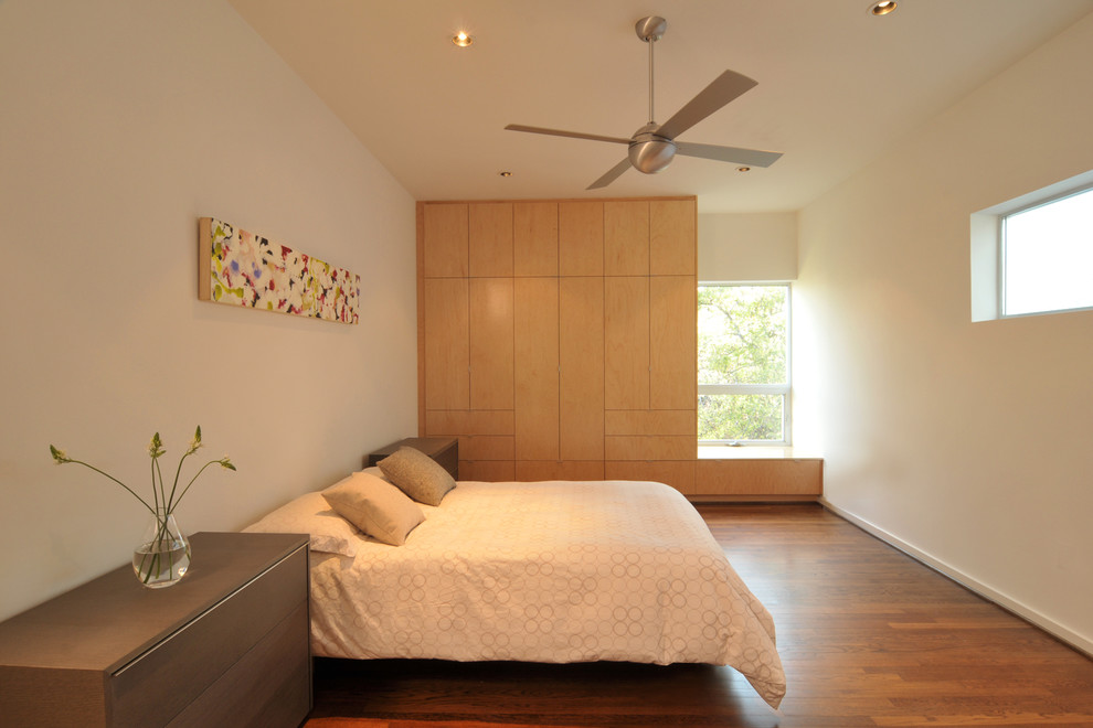 This is an example of a modern bedroom in Houston with beige walls and medium hardwood floors.
