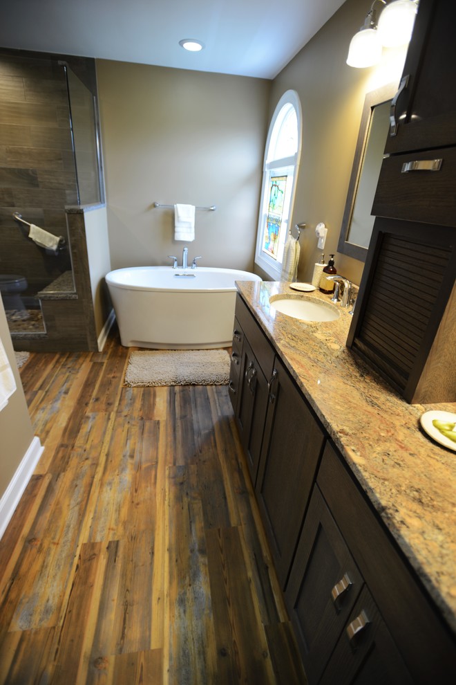 Photo of a mid-sized country master bathroom in Baltimore with shaker cabinets, medium wood cabinets, a freestanding tub, a corner shower, brown tile, beige walls, vinyl floors, a drop-in sink and granite benchtops.
