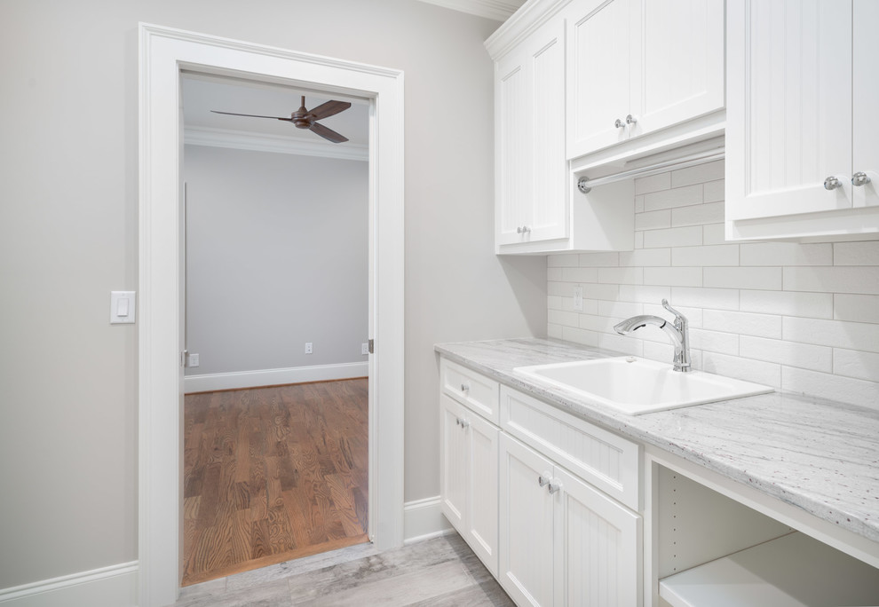 Photo of a large transitional dedicated laundry room in Other with a drop-in sink, white cabinets, quartz benchtops, grey walls, dark hardwood floors, grey floor and recessed-panel cabinets.