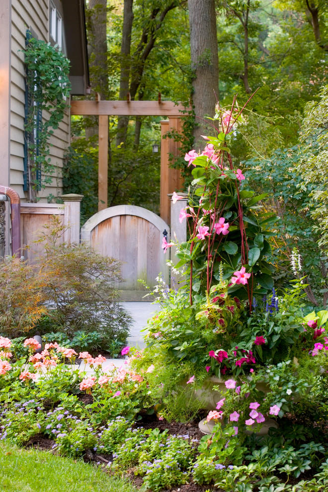 Imagen de jardín mediterráneo grande en verano en patio lateral con parterre de flores, exposición parcial al sol, adoquines de piedra natural y con madera