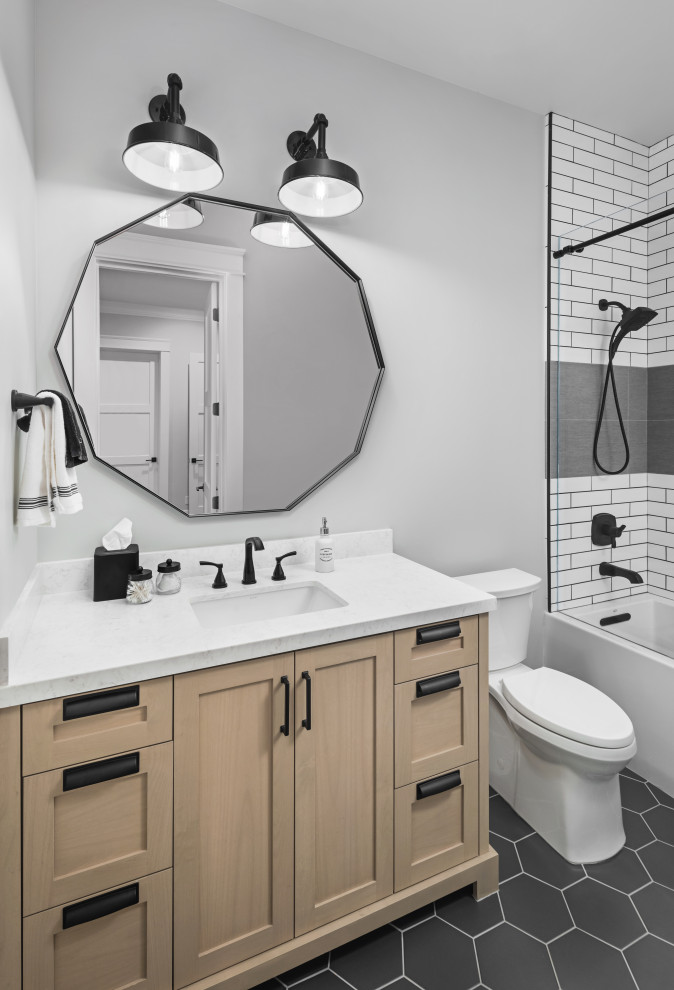 This is an example of a mid-sized country bathroom in Phoenix with shaker cabinets, light wood cabinets, a shower/bathtub combo, a two-piece toilet, white tile, porcelain tile, grey walls, porcelain floors, an undermount sink, solid surface benchtops, black floor, a sliding shower screen, white benchtops, a single vanity and a built-in vanity.
