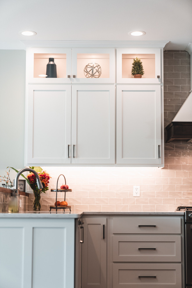 Large transitional l-shaped vinyl floor and brown floor kitchen pantry photo with an undermount sink, shaker cabinets, white cabinets, quartz countertops, gray backsplash, subway tile backsplash, stainless steel appliances, an island and white countertops
