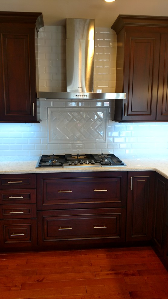 Large transitional u-shaped medium tone wood floor kitchen photo in New York with an undermount sink, raised-panel cabinets, dark wood cabinets, white backsplash, subway tile backsplash, stainless steel appliances and a peninsula