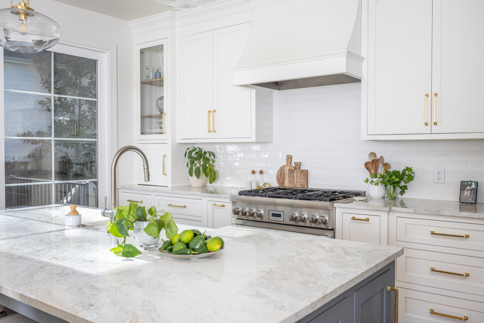 Design ideas for a mid-sized transitional open plan kitchen in Raleigh with a farmhouse sink, shaker cabinets, white cabinets, white splashback, subway tile splashback, stainless steel appliances, medium hardwood floors, with island, brown floor, multi-coloured benchtop and quartzite benchtops.
