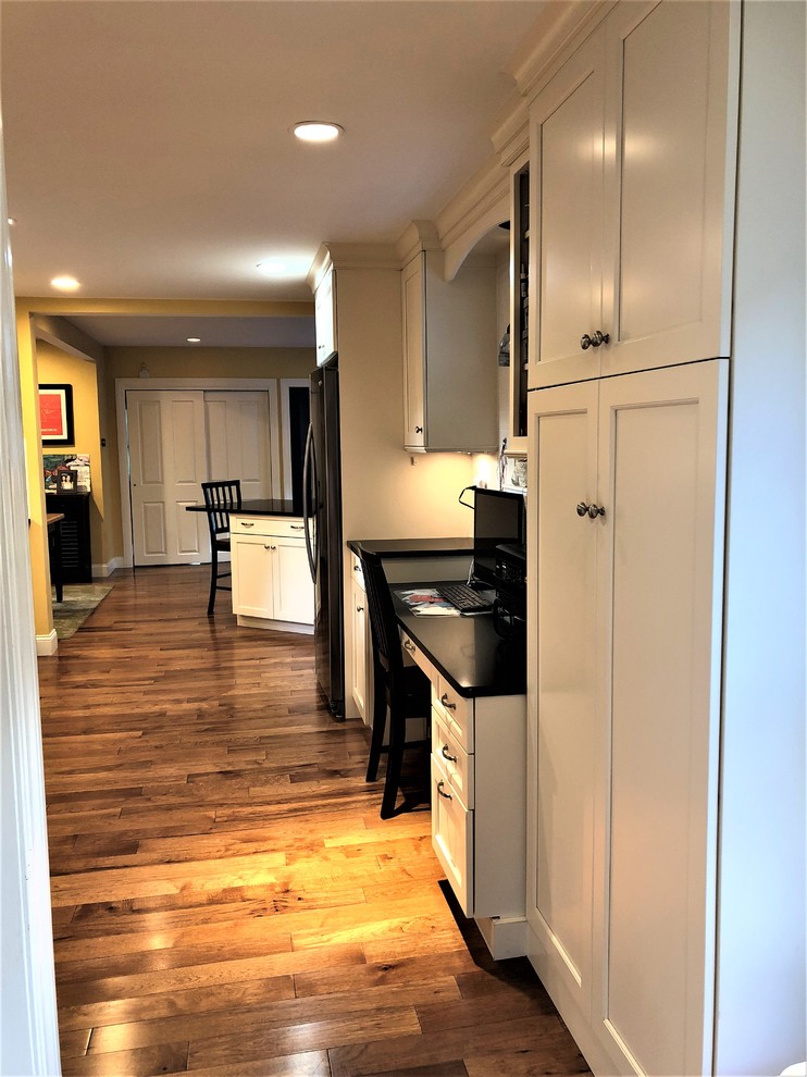 Enclosed kitchen - small transitional galley medium tone wood floor and brown floor enclosed kitchen idea in Boston with an undermount sink, shaker cabinets, white cabinets, granite countertops, white backsplash, subway tile backsplash, stainless steel appliances and black countertops