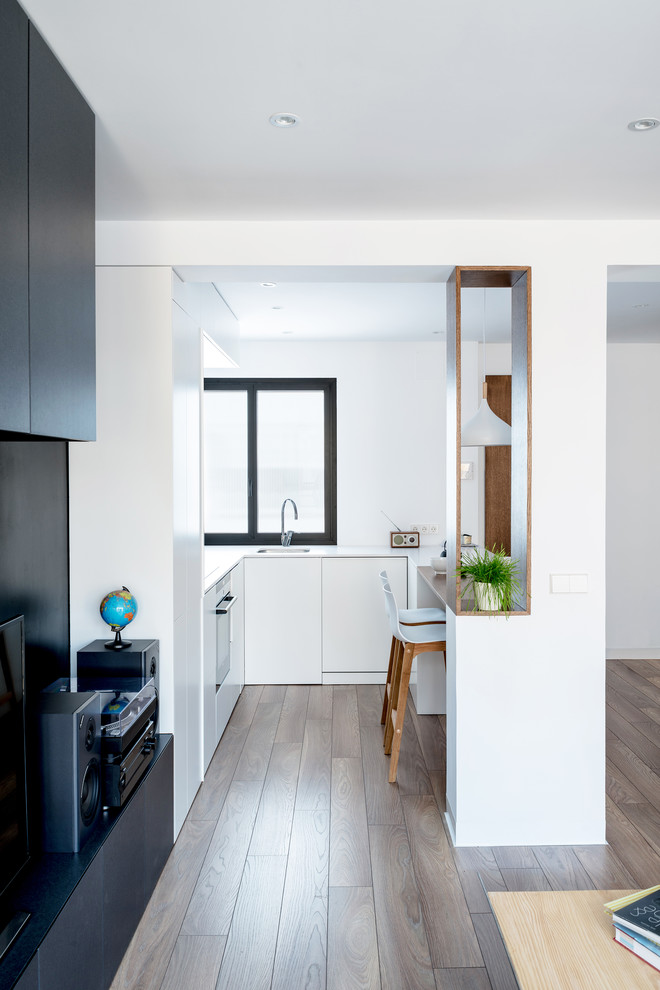 This is an example of a small modern u-shaped open plan kitchen in Madrid with a drop-in sink, flat-panel cabinets, medium wood cabinets, quartz benchtops, white splashback, panelled appliances, medium hardwood floors, a peninsula and brown floor.