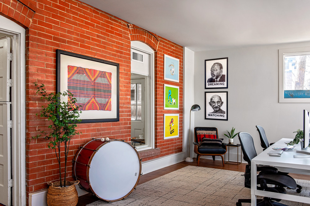 Photo of an eclectic home office in Denver with white walls, brown floor, dark hardwood floors, a freestanding desk and brick walls.