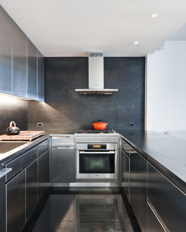 Photo of a small contemporary galley eat-in kitchen in New York with stainless steel cabinets, stainless steel benchtops, an undermount sink, flat-panel cabinets, black splashback, metal splashback, stainless steel appliances, dark hardwood floors and a peninsula.