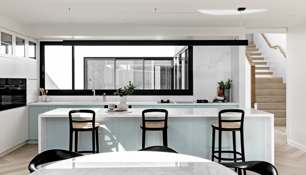 This is an example of a contemporary l-shaped kitchen in Sydney with turquoise cabinets, quartz benchtops, engineered quartz splashback, with island, white benchtop, a drop-in sink, flat-panel cabinets, white splashback, light hardwood floors and beige floor.