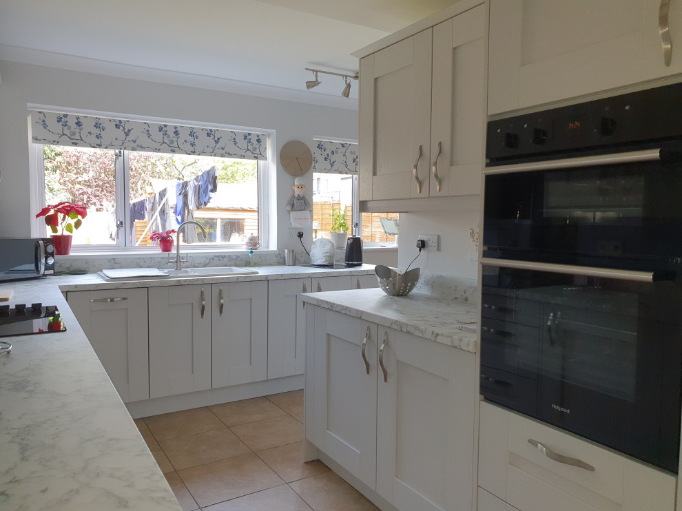Photo of a medium sized contemporary grey and purple u-shaped kitchen/diner in West Midlands with a double-bowl sink, shaker cabinets, grey cabinets, laminate countertops, black splashback, glass tiled splashback, black appliances, terracotta flooring, no island, brown floors, multicoloured worktops and a coffered ceiling.