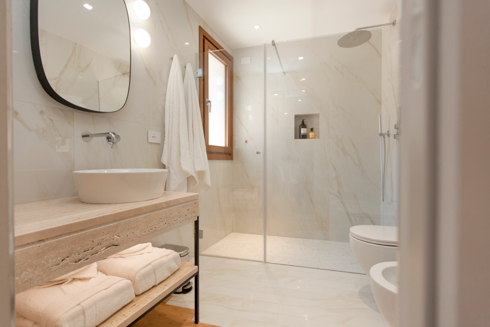 Modern inredning av ett stort beige beige badrum med dusch, med öppna hyllor, beige skåp, en kantlös dusch, en toalettstol med separat cisternkåpa, beige kakel, porslinskakel, beige väggar, bambugolv, ett fristående handfat, marmorbänkskiva, beiget golv och dusch med gångjärnsdörr