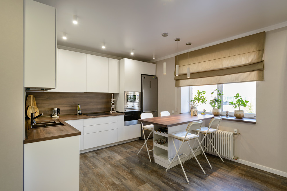 This is an example of a large contemporary l-shaped open plan kitchen in Novosibirsk with a drop-in sink, flat-panel cabinets, white cabinets, wood benchtops, brown splashback, timber splashback, stainless steel appliances, vinyl floors, with island, brown floor and brown benchtop.