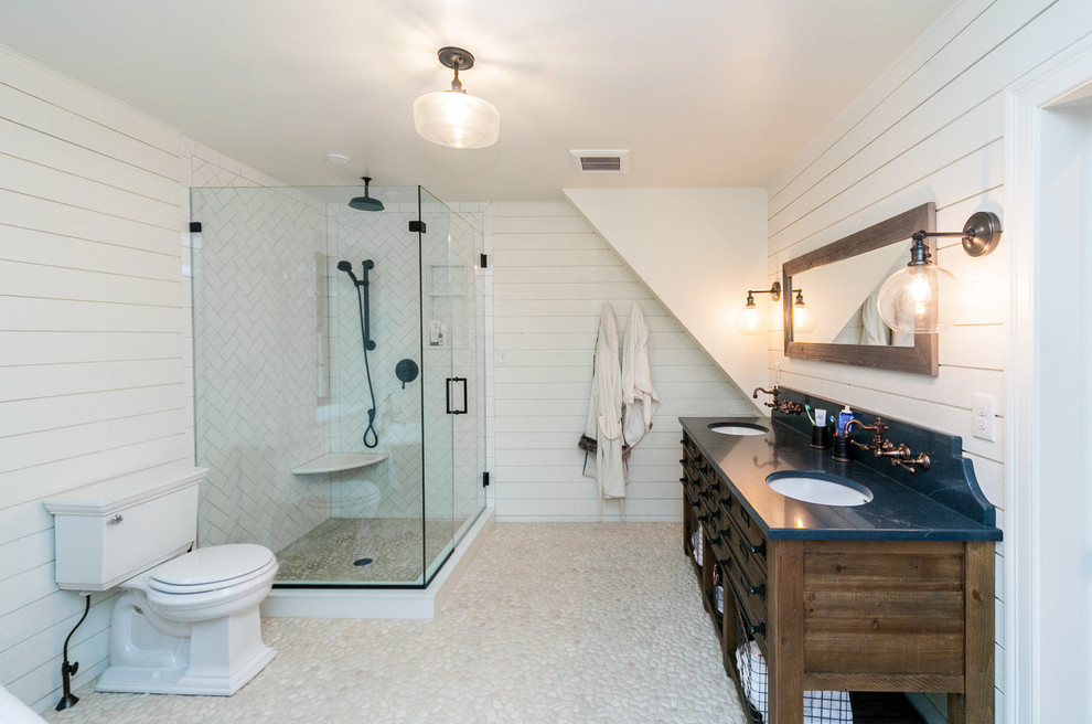 This is an example of a large country master bathroom in Other with furniture-like cabinets, medium wood cabinets, a corner shower, a two-piece toilet, porcelain tile, white walls, pebble tile floors, an undermount sink, soapstone benchtops, beige floor, a hinged shower door and blue benchtops.