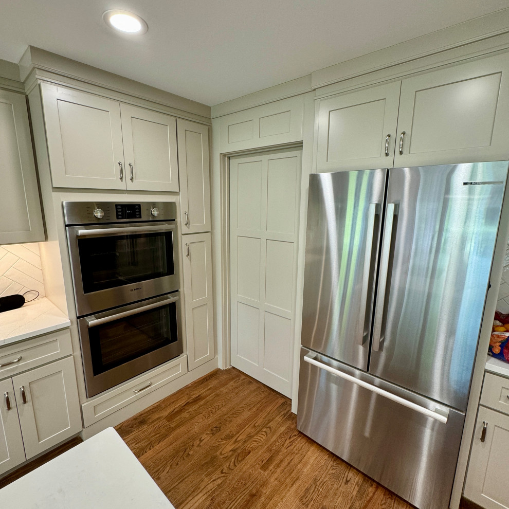 Mid-sized transitional l-shaped medium tone wood floor, brown floor and wallpaper ceiling eat-in kitchen photo in Atlanta with an undermount sink, shaker cabinets, white cabinets, granite countertops, white backsplash, stainless steel appliances, an island and white countertops