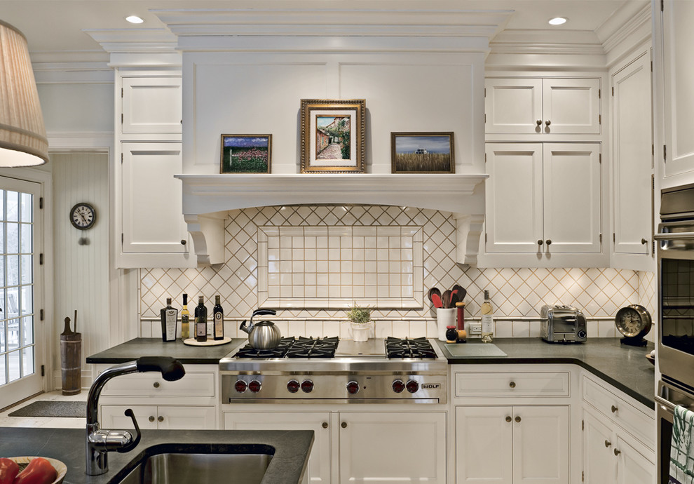 This is an example of a country eat-in kitchen in New York with soapstone benchtops, a drop-in sink, beaded inset cabinets, white cabinets, white splashback, porcelain splashback and stainless steel appliances.