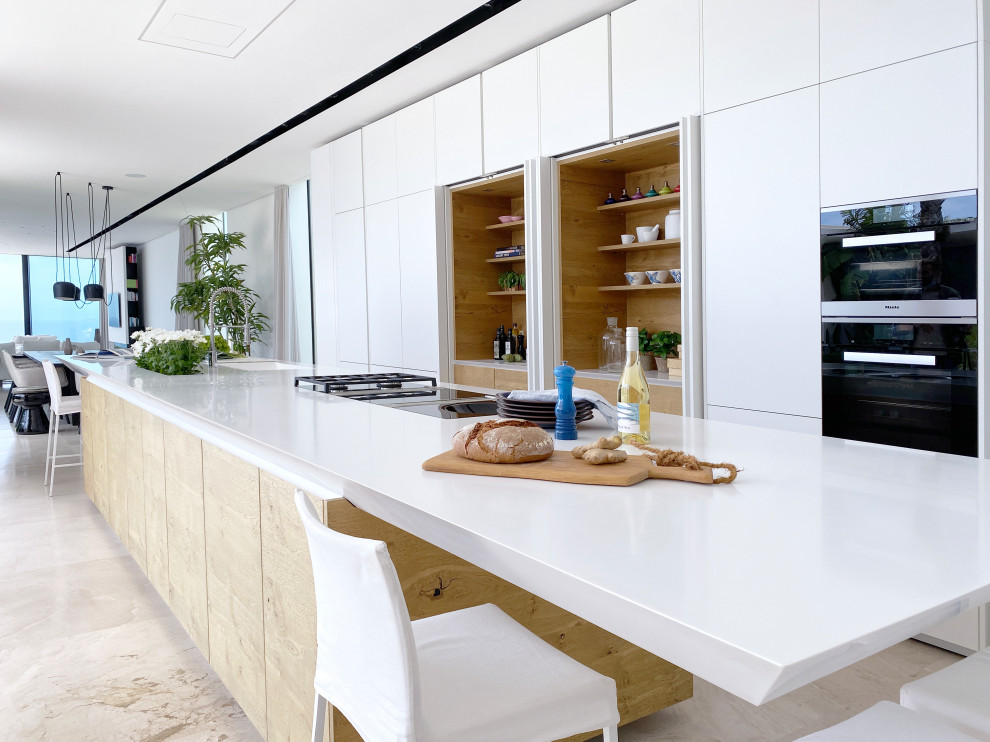 Inspiration for an expansive mediterranean single-wall open plan kitchen in Palma de Mallorca with an undermount sink, recessed-panel cabinets, white cabinets, laminate benchtops, white splashback, metal splashback, panelled appliances, travertine floors, with island, beige floor and white benchtop.