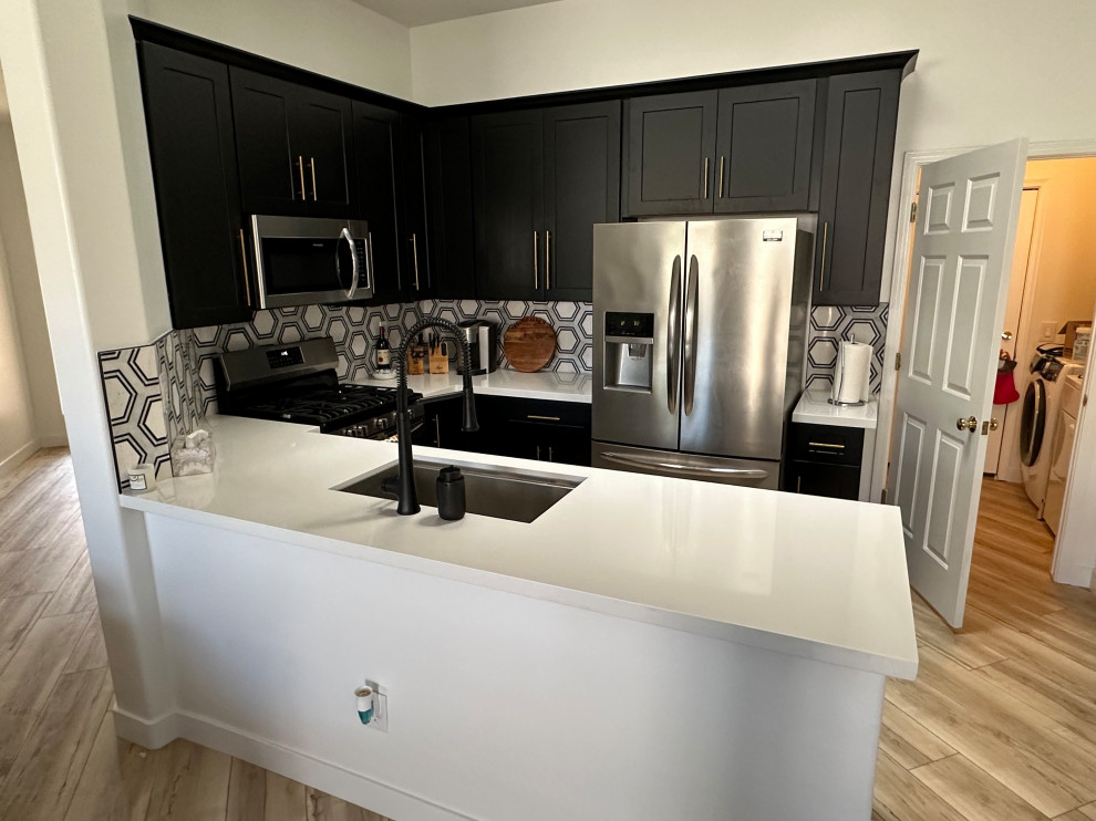 This is an example of a mid-sized modern u-shaped eat-in kitchen in Phoenix with a single-bowl sink, shaker cabinets, black cabinets, quartz benchtops, black splashback, marble splashback, stainless steel appliances, laminate floors, a peninsula, beige floor and white benchtop.