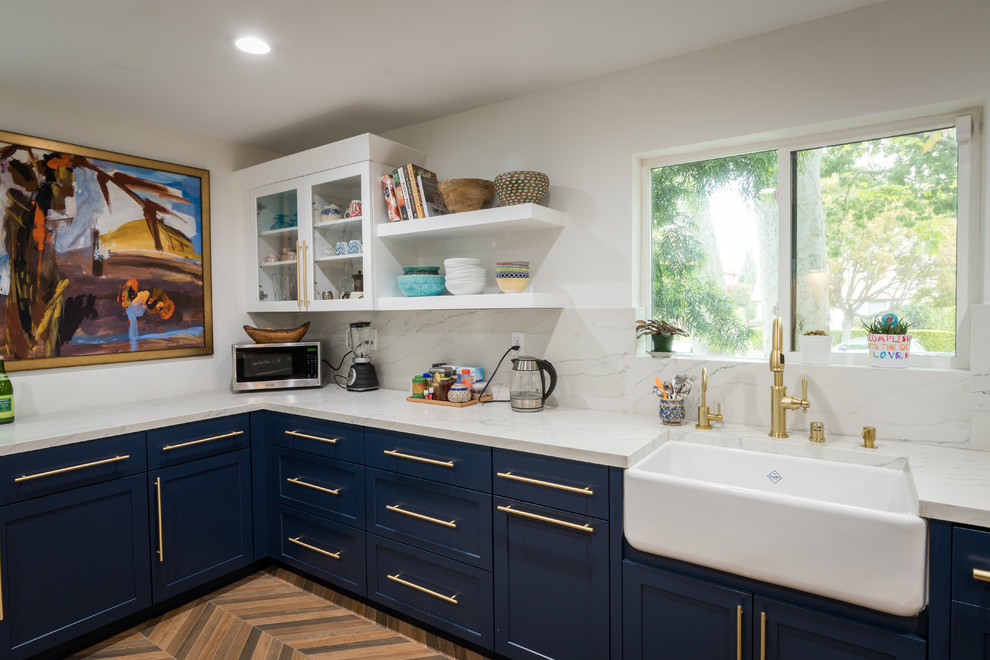 Mid-sized traditional l-shaped eat-in kitchen in Los Angeles with a farmhouse sink, shaker cabinets, blue cabinets, quartz benchtops, white splashback, marble splashback, stainless steel appliances, medium hardwood floors, a peninsula, beige floor and white benchtop.
