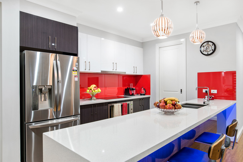 Contemporary galley kitchen in Melbourne with an undermount sink, flat-panel cabinets, dark wood cabinets, red splashback, glass sheet splashback, stainless steel appliances, medium hardwood floors and a peninsula.
