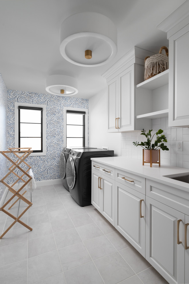Design ideas for a large traditional single-wall dedicated laundry room in Detroit with an undermount sink, shaker cabinets, white cabinets, quartz benchtops, white splashback, subway tile splashback, white walls, ceramic floors, a side-by-side washer and dryer, grey floor, white benchtop and wallpaper.