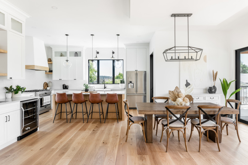 Photo of an expansive country kitchen/dining combo in Vancouver with white walls, light hardwood floors, a hanging fireplace, a metal fireplace surround and beige floor.