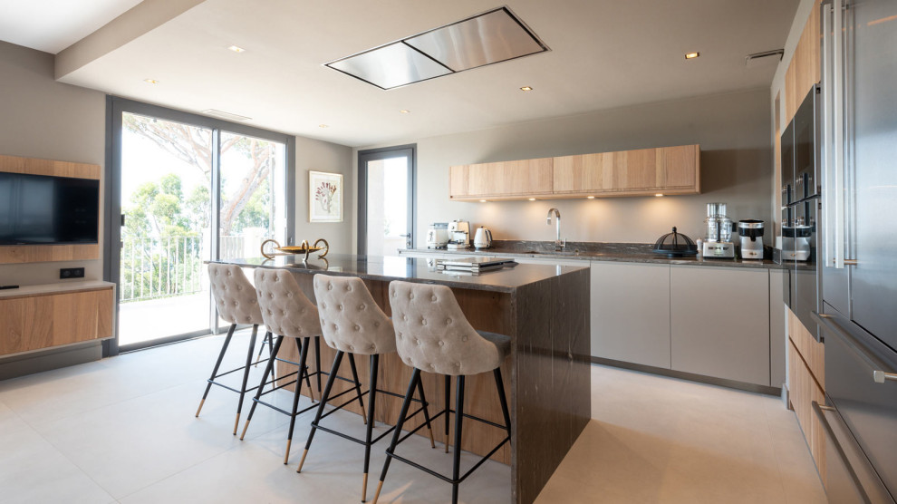 Large contemporary l-shaped eat-in kitchen in Marseille with an undermount sink, beaded inset cabinets, beige cabinets, granite benchtops, beige splashback, black appliances, ceramic floors, with island, beige floor and brown benchtop.
