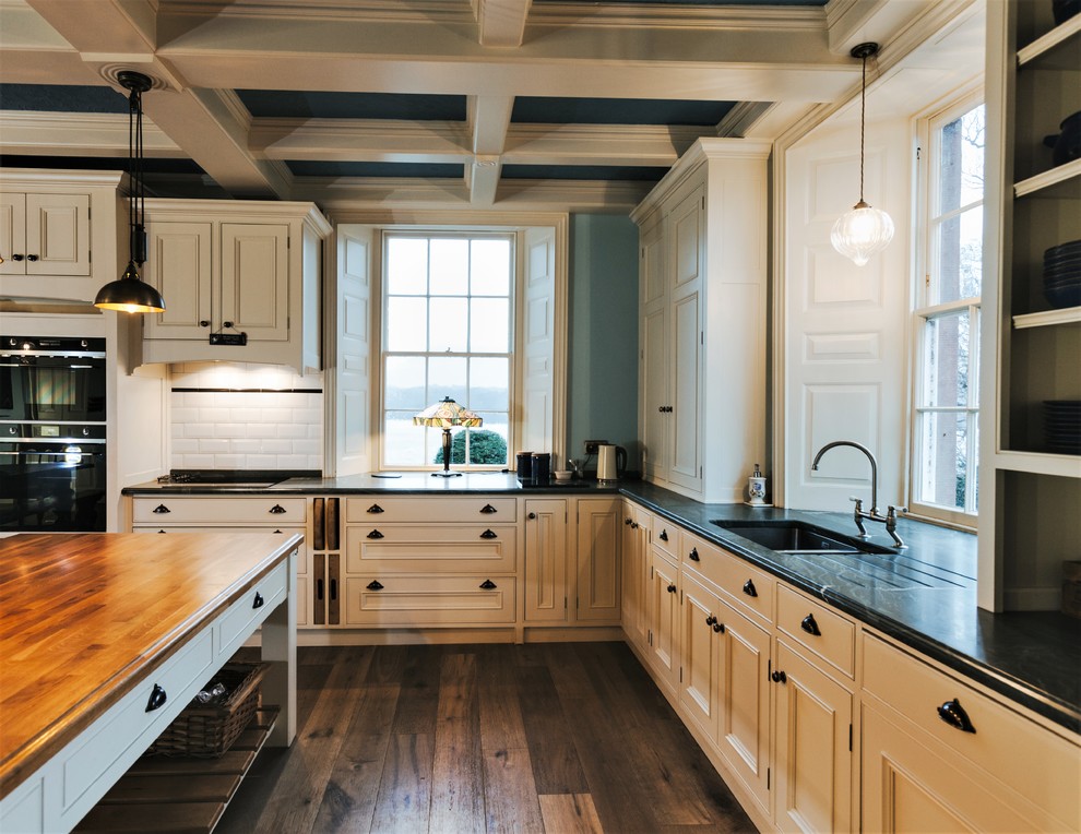 Inspiration for an expansive traditional u-shaped eat-in kitchen in Wiltshire with a double-bowl sink, beaded inset cabinets, white cabinets, granite benchtops, green splashback, black appliances, dark hardwood floors, with island, green benchtop and stone slab splashback.