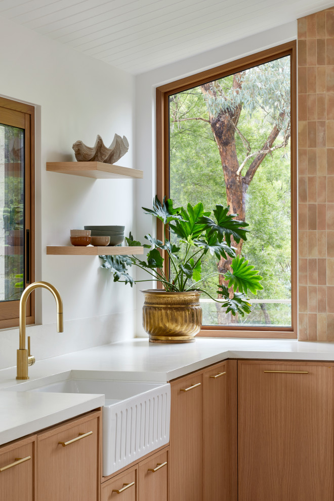 Inredning av ett modernt stort vit vitt u-kök, med en rustik diskho, skåp i shakerstil, skåp i mellenmörkt trä, rosa stänkskydd, stänkskydd i porslinskakel, svarta vitvaror, mellanmörkt trägolv, en köksö och brunt golv