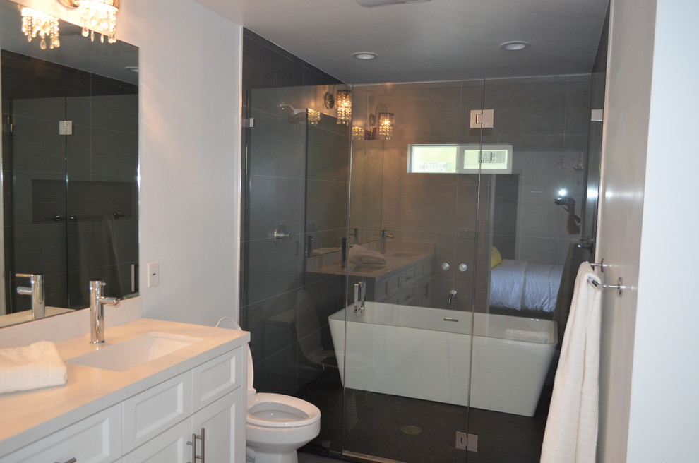 Photo of a mid-sized traditional master bathroom in Los Angeles with recessed-panel cabinets, white cabinets, a freestanding tub, an alcove shower, a one-piece toilet, gray tile, ceramic tile, grey walls, an undermount sink, concrete benchtops, a hinged shower door and white benchtops.