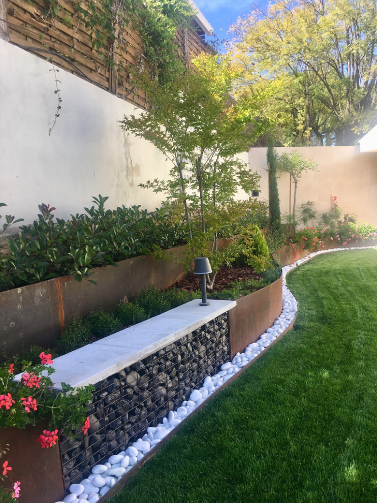 Cette photo montre un jardin méditerranéen de taille moyenne avec une bordure, une exposition partiellement ombragée, des pavés en pierre naturelle et une clôture en métal.