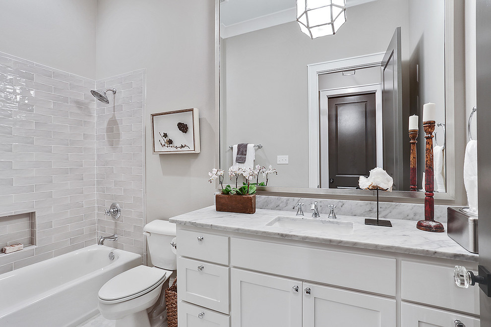Inspiration for a mid-sized traditional bathroom in New Orleans with recessed-panel cabinets, white cabinets, an alcove tub, a shower/bathtub combo, a one-piece toilet, multi-coloured tile, porcelain tile, grey walls, medium hardwood floors, a drop-in sink and marble benchtops.