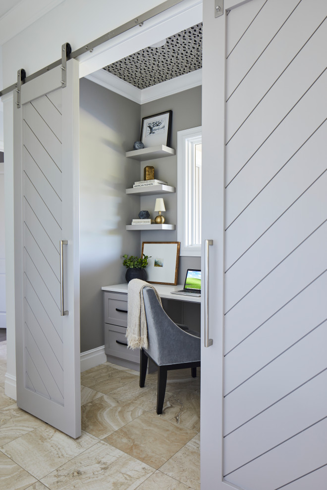 This is an example of a small transitional study room in Other with grey walls, travertine floors, a built-in desk, beige floor and wallpaper.