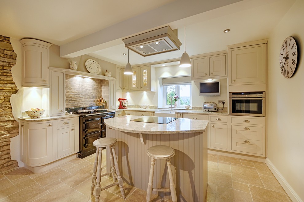 Inspiration for a large traditional l-shaped eat-in kitchen in Manchester with a farmhouse sink, recessed-panel cabinets, beige cabinets, granite benchtops, brown splashback, porcelain splashback, stainless steel appliances, limestone floors and with island.