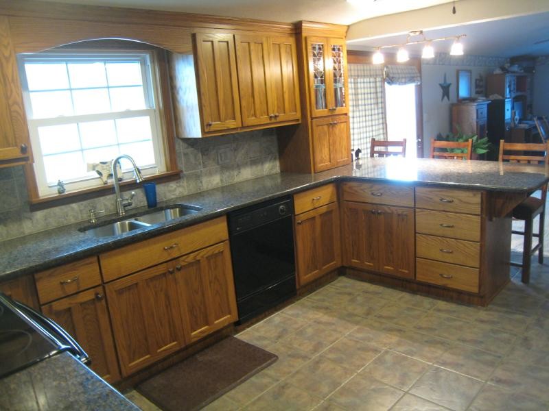 Example of a mid-sized classic u-shaped ceramic tile and gray floor enclosed kitchen design with a double-bowl sink, shaker cabinets, dark wood cabinets, granite countertops, gray backsplash, stone tile backsplash, black appliances and a peninsula
