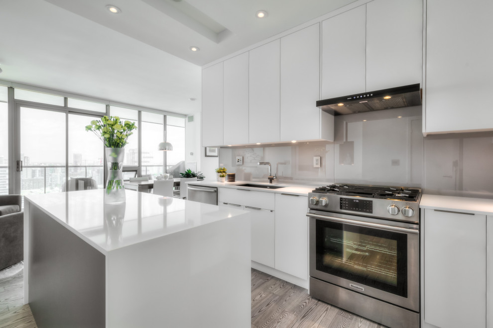 Inspiration for a small modern galley eat-in kitchen in Toronto with an undermount sink, flat-panel cabinets, white cabinets, quartz benchtops, grey splashback, glass sheet splashback, stainless steel appliances, medium hardwood floors, with island, grey floor, white benchtop and coffered.