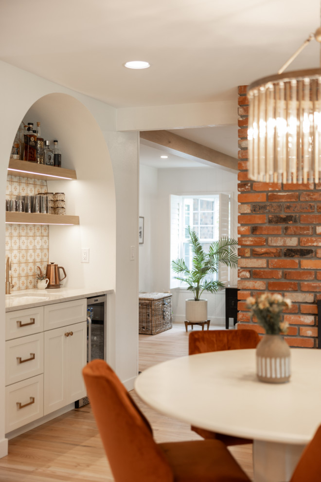 This is an example of a large kitchen/dining combo in Denver with white walls, a two-sided fireplace, a brick fireplace surround and light hardwood floors.