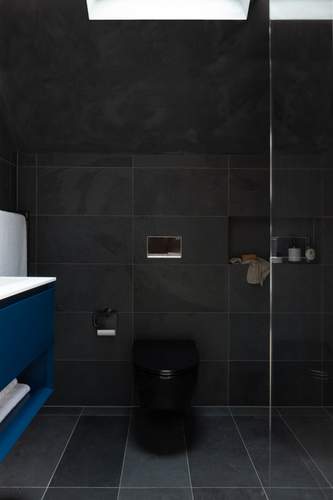 Design ideas for a small modern bathroom in London with flat-panel cabinets, blue cabinets, a wall mounted toilet, black tiles, porcelain tiles, a built-in sink, solid surface worktops, black floors, an open shower, white worktops, a single sink and a freestanding vanity unit.