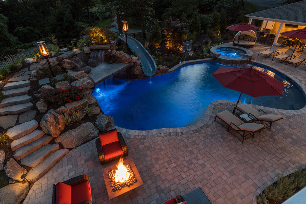 This is an example of a mid-sized country backyard custom-shaped pool in New York with a water slide and brick pavers.