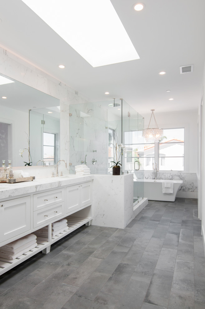 Inspiration for a large beach style master bathroom in Orange County with an undermount sink, furniture-like cabinets, white cabinets, marble benchtops, a freestanding tub, white tile, stone tile, white walls and limestone floors.