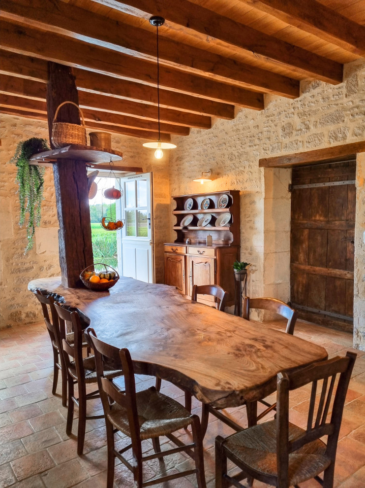 Exemple d'une salle à manger nature fermée et de taille moyenne avec un mur beige, tomettes au sol, une cheminée standard, un manteau de cheminée en pierre de parement, un sol rouge et poutres apparentes.