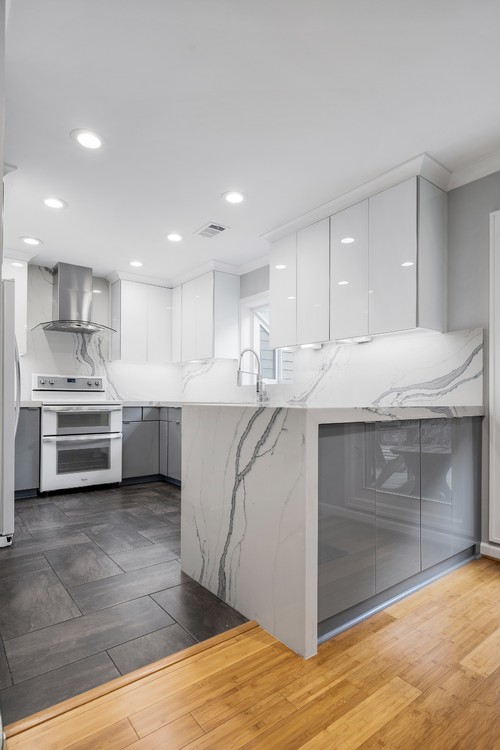 Modern kitchen with high-gloss white wall cabinets, gray base units, and a waterfall quartz peninsula after professional installation