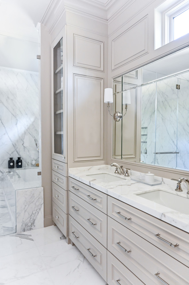 Large elegant master gray tile and marble tile marble floor, white floor, single-sink and wall paneling wet room photo in Houston with raised-panel cabinets, beige cabinets, an undermount tub, a two-piece toilet, beige walls, an undermount sink, marble countertops, a hinged shower door, white countertops and a built-in vanity