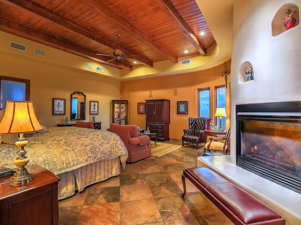 Design ideas for a mid-sized master bedroom in Albuquerque with yellow walls, slate floors, a standard fireplace, a plaster fireplace surround and multi-coloured floor.
