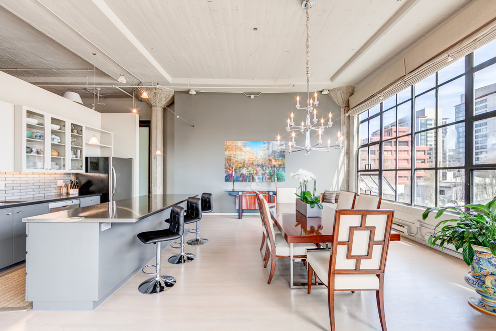 This is an example of an industrial open plan dining in San Francisco with grey walls and light hardwood floors.