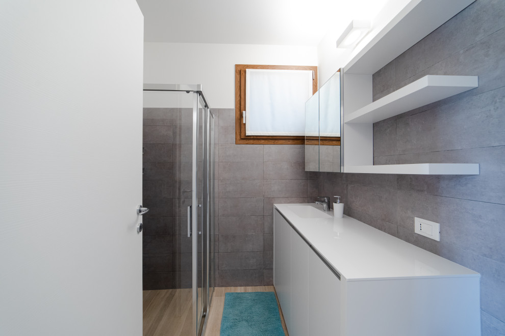 Inspiration for a small modern galley utility room in Milan with a drop-in sink, flat-panel cabinets, white cabinets, quartz benchtops, grey splashback, cement tile splashback, grey walls, porcelain floors, a concealed washer and dryer, beige floor and white benchtop.