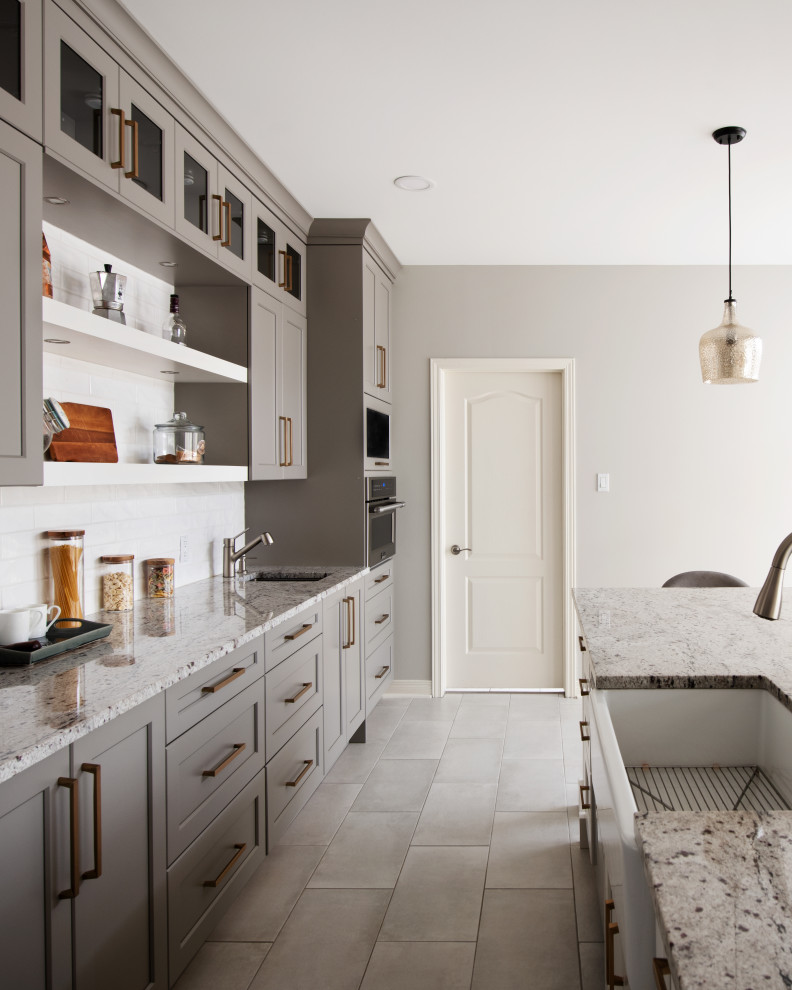 Open concept kitchen - mid-sized transitional l-shaped porcelain tile and gray floor open concept kitchen idea in Ottawa with a farmhouse sink, shaker cabinets, gray cabinets, granite countertops, white backsplash, ceramic backsplash, stainless steel appliances, an island and multicolored countertops