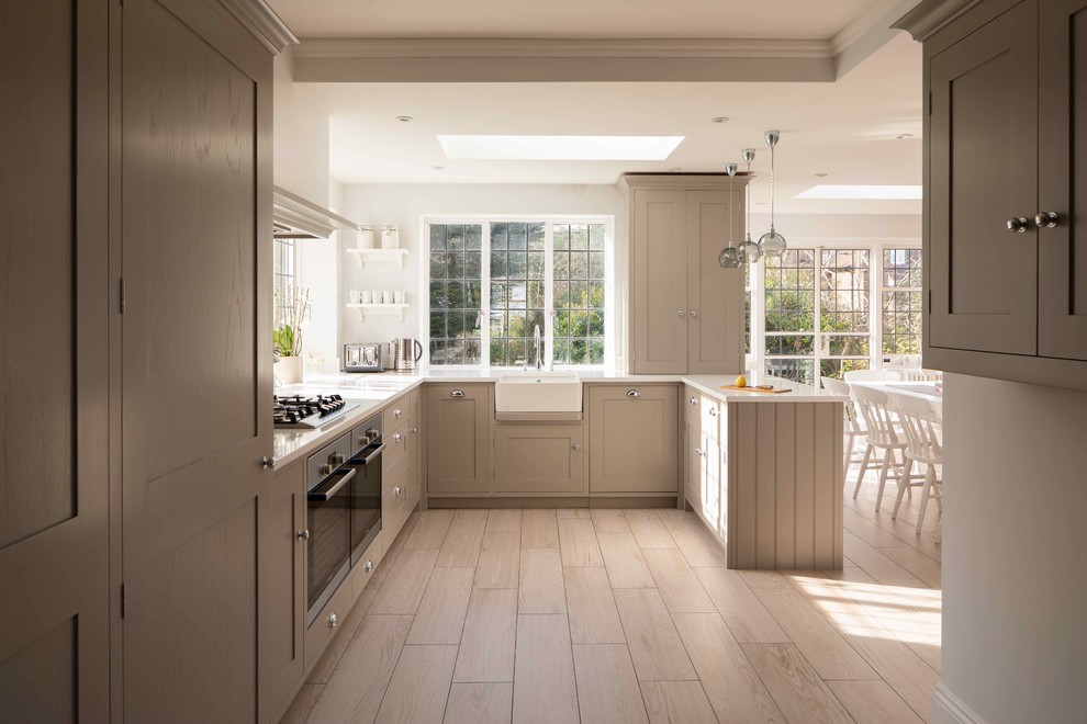 Design ideas for a mid-sized country u-shaped kitchen in London with a farmhouse sink, recessed-panel cabinets, beige cabinets, stainless steel appliances and beige floor.