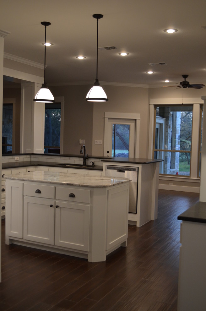 Design ideas for a mid-sized arts and crafts u-shaped eat-in kitchen in Austin with a drop-in sink, recessed-panel cabinets, white cabinets, granite benchtops, white splashback, ceramic splashback, stainless steel appliances, porcelain floors and with island.