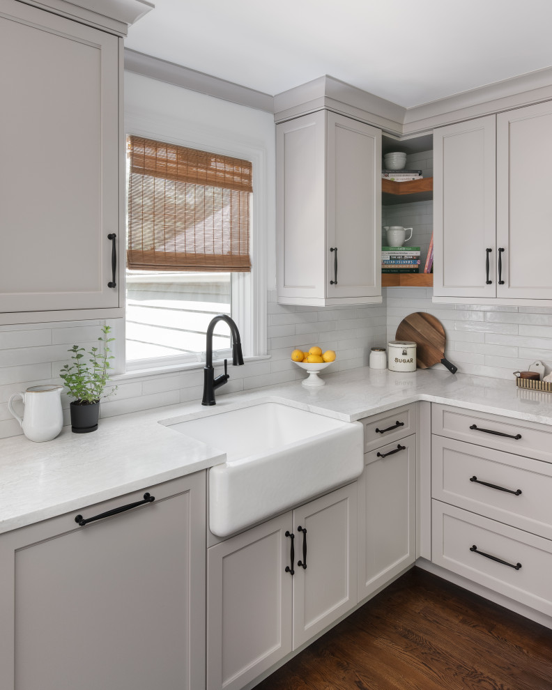 Inspiration for a mid-sized transitional l-shaped medium tone wood floor and brown floor eat-in kitchen remodel in New York with a farmhouse sink, shaker cabinets, beige cabinets, quartz countertops, white backsplash, porcelain backsplash, paneled appliances, an island and white countertops