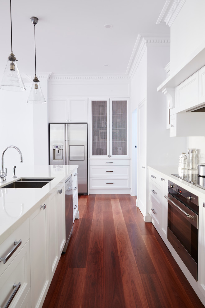 Photo of a large traditional u-shaped kitchen in Sydney with a double-bowl sink, recessed-panel cabinets, white cabinets, white splashback, ceramic splashback, stainless steel appliances, medium hardwood floors and with island.